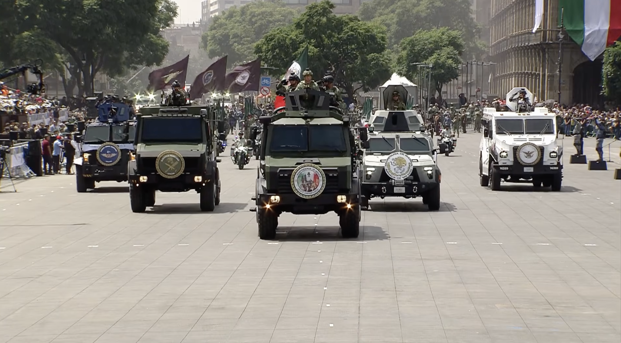 Convoy de vehículos blindados tácticos de las Fuerzas Armadas de México (Ejército, Marina, Fuerza Aérea y Guardia Nacional) desplazándose en formación sobre la Plaza de la Constitución, saludando a las autoridades y asistentes durante la conmemoración del 216 aniversario del inicio de la Independencia de México