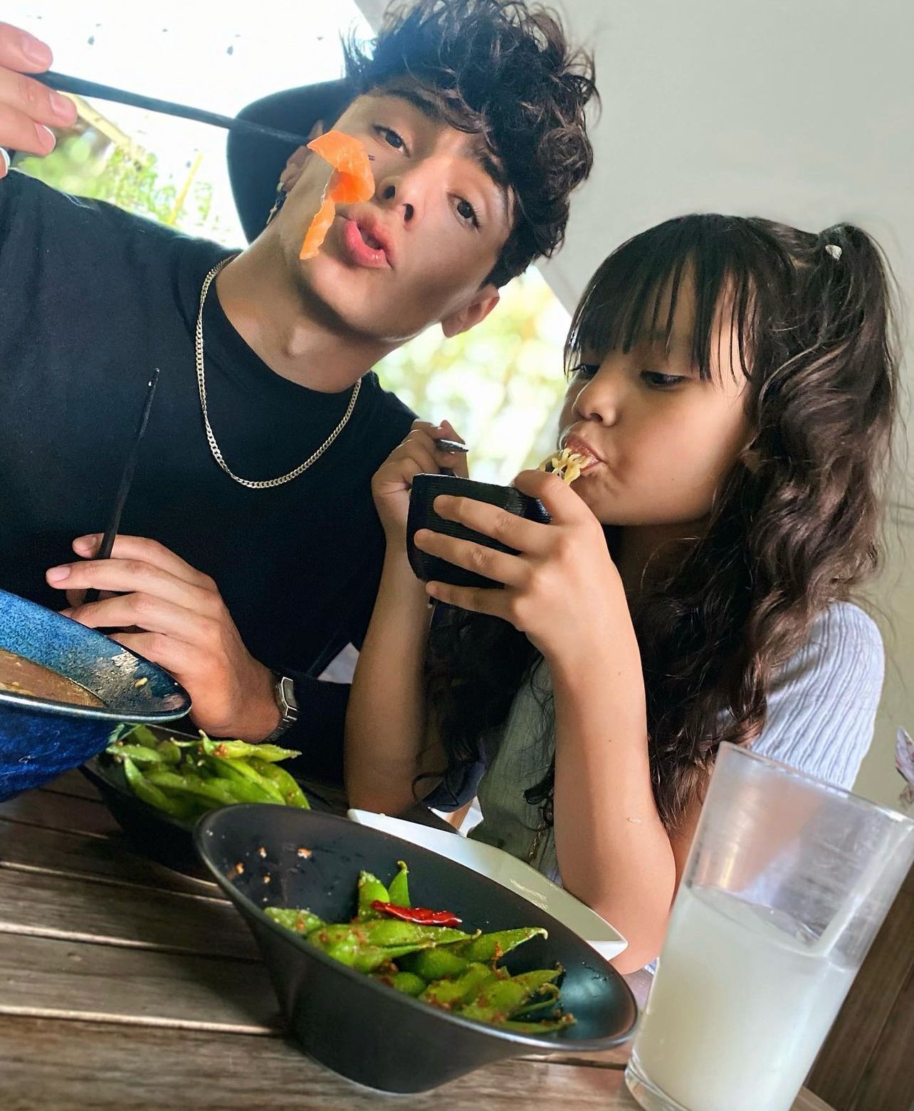 Betin y Flowsito disfrutan de una comida de vegetales, pasta y Salmón, mientras él muestra un trozo de pescado en un palillo chino y su hija sorbe pasta de un tazón. 
 