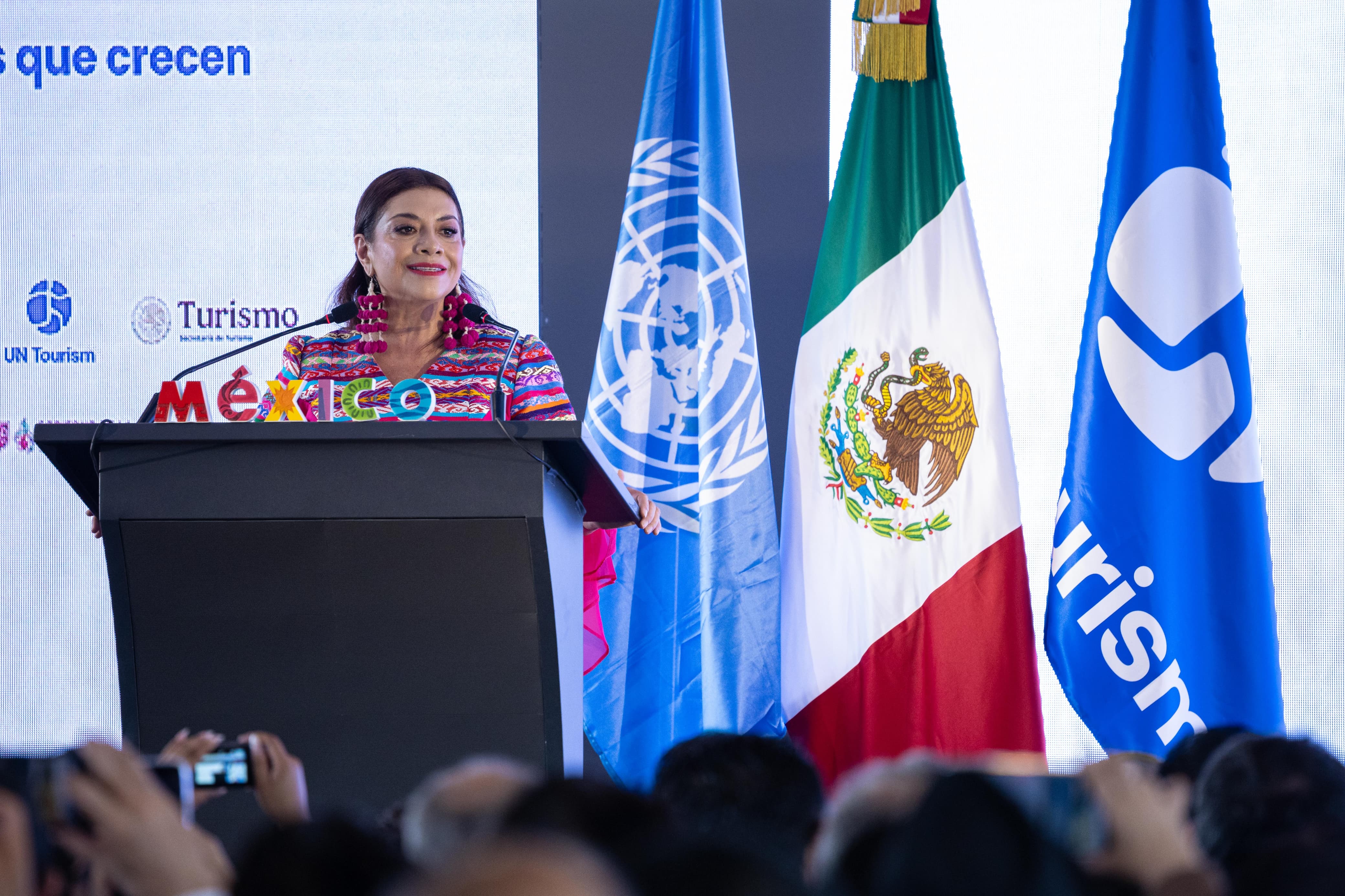La jefa de gobierno, Clara Brugada da un discurso a los asistentes al foro de turismos mundial, de fondo están las banderas de México y la ONU