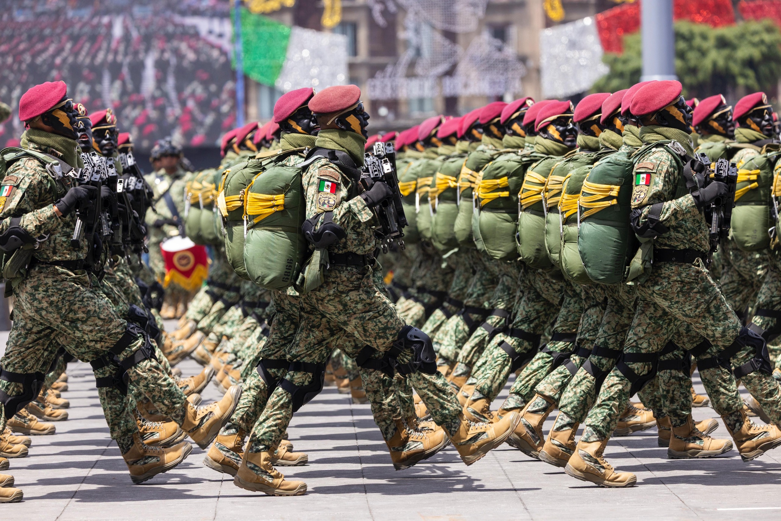 Contingente de la Brigada de Fusileros Paracaidistas portando boinas rojas, equipo táctico de salto y rostros camuflados, marchando en paso redoblado durante el Desfile Militar en el Zócalo de la Ciudad de México.