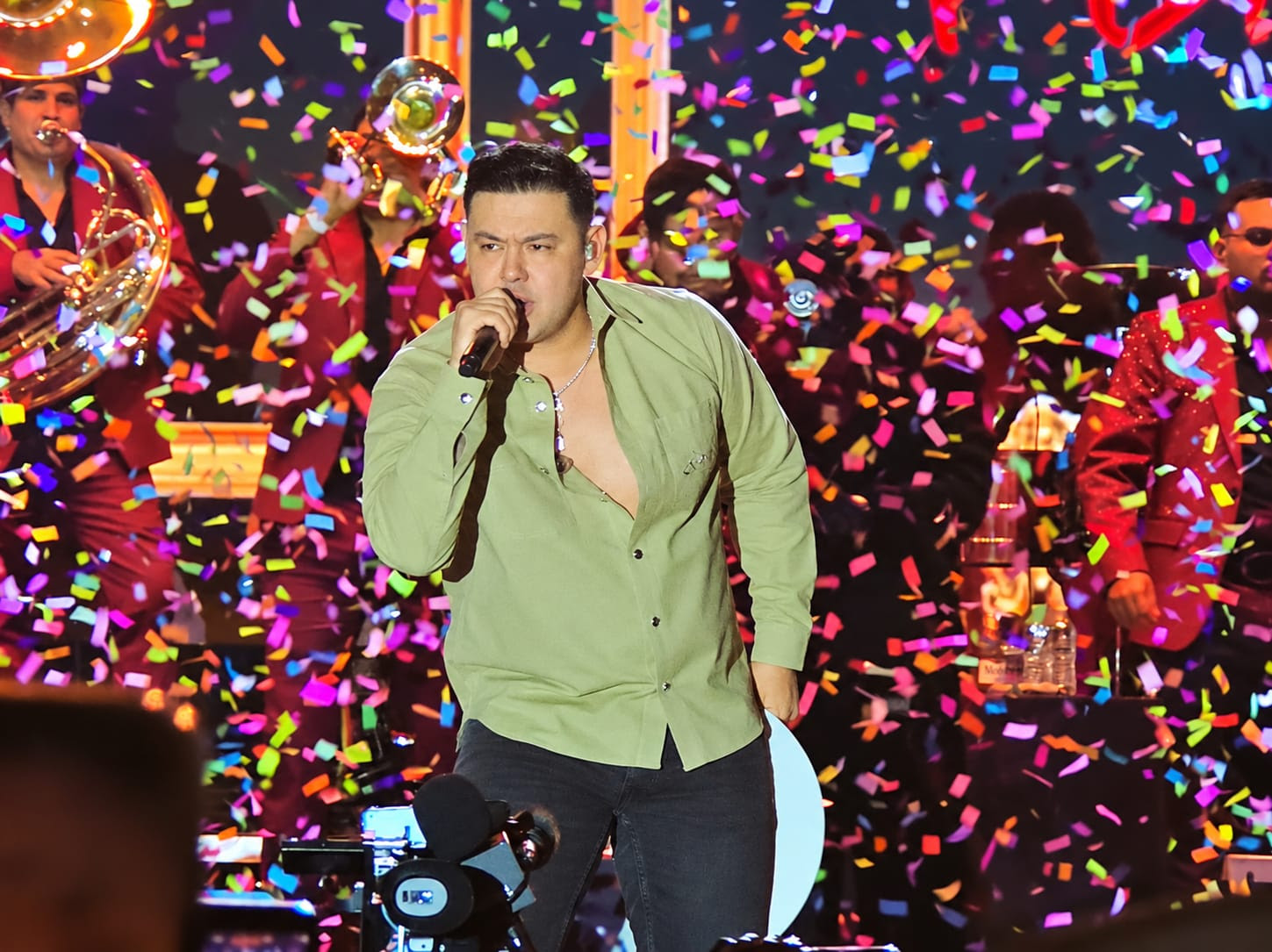 El cantante de música regional mexicana Luis Alfonso Partida “El Yaki” interpreta un tema en el escenario durante la celebración de las Fiestas Patrias en La Magdalena Contreras, rodeado de confeti multicolor y respaldado por su banda de músicos.