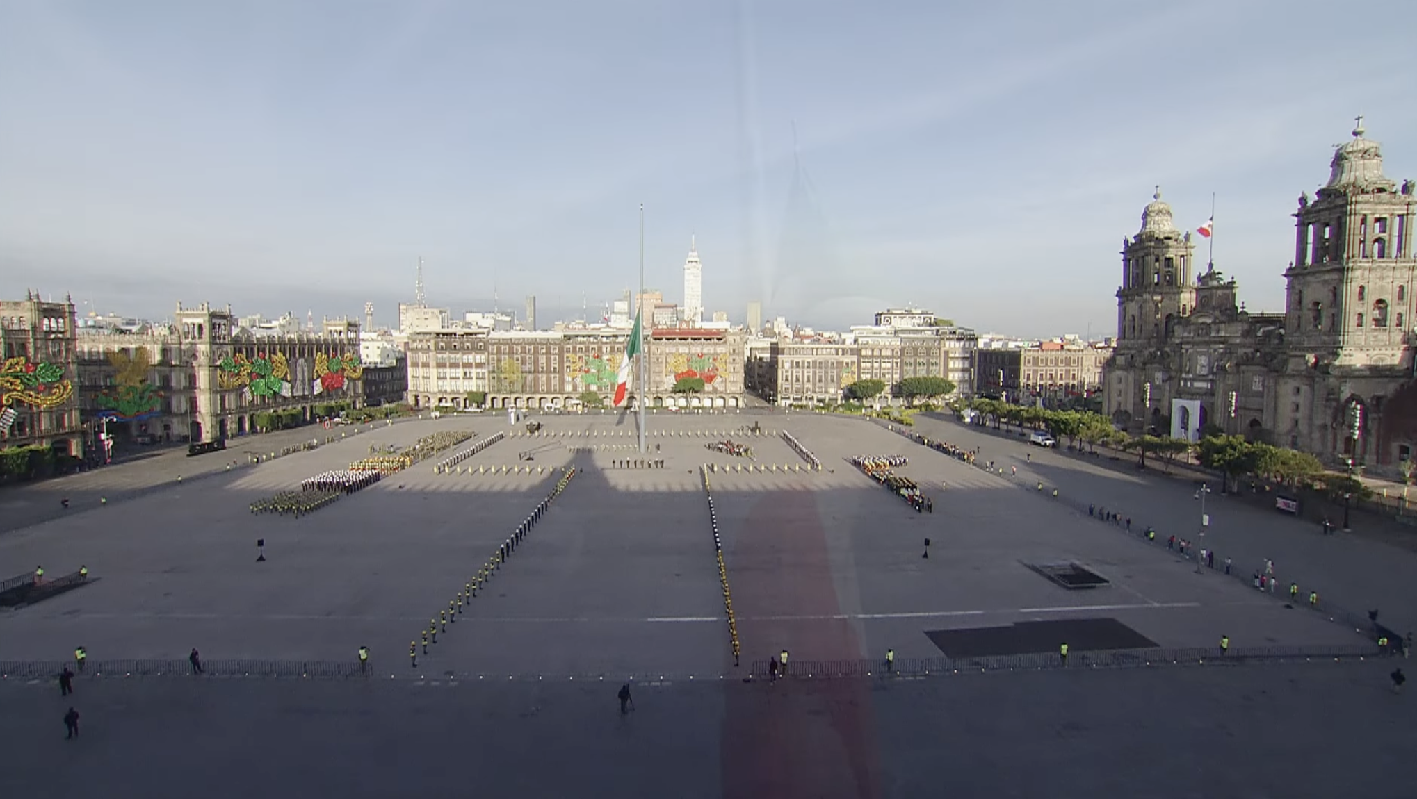 Vista aérea del Zócalo de la Ciudad de México con la bandera mexicana a media asta, personal militar e instalaciones formadas en la explanada, y la Catedral Metropolitana a la derecha