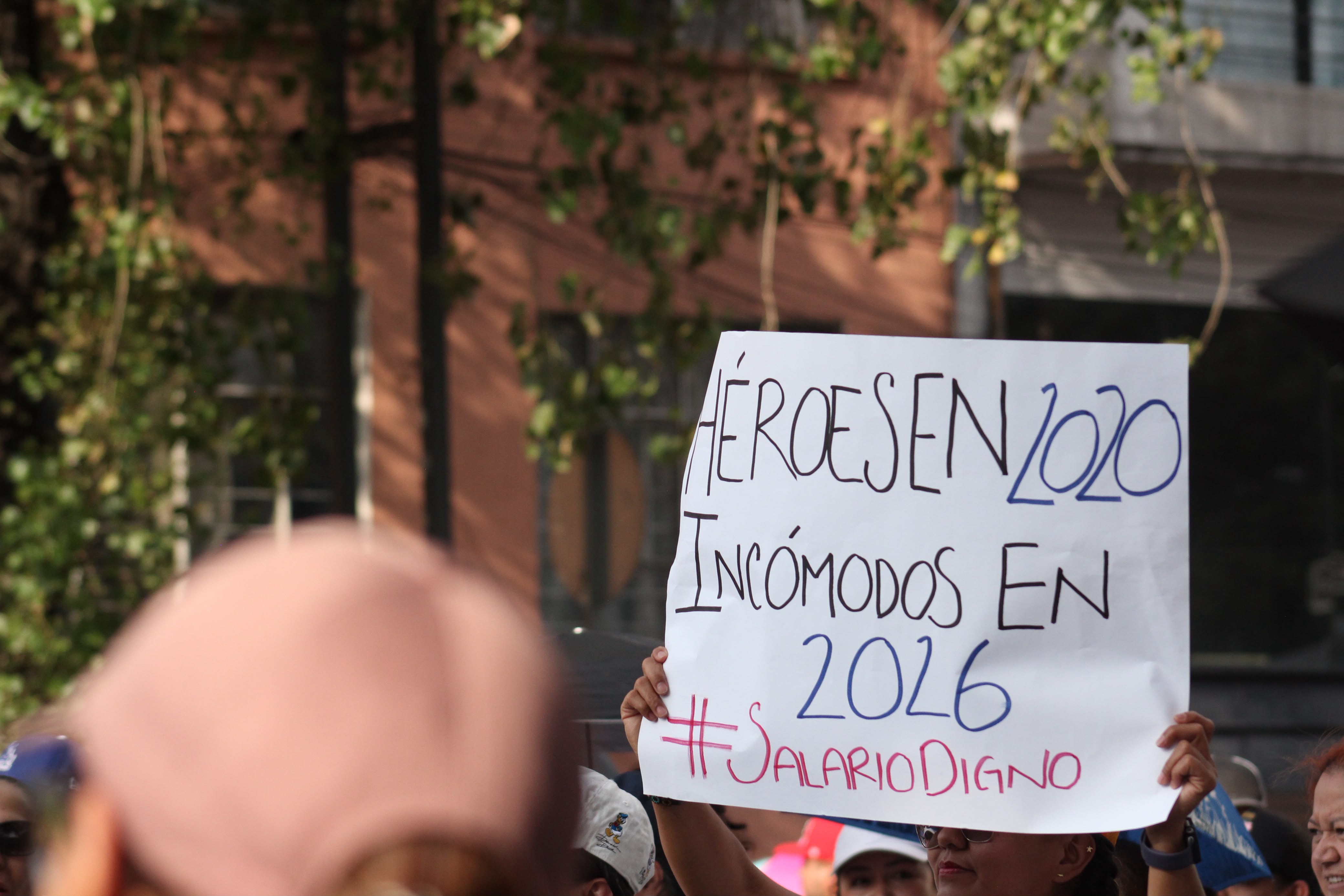 Pancarta de protesta escrita a mano que dice: "HÉROES EN 2020. INCÓMODOS EN 2026. #SALARIODIGNO", sostenida sobre una multitud.