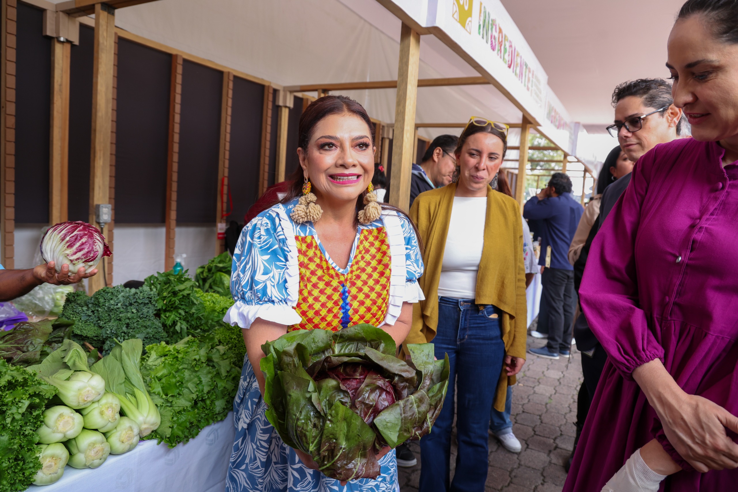 Clara Brugada sostiene una lechuga fresca en el evento Ingrediente con productores agrícolas de la CDMX.